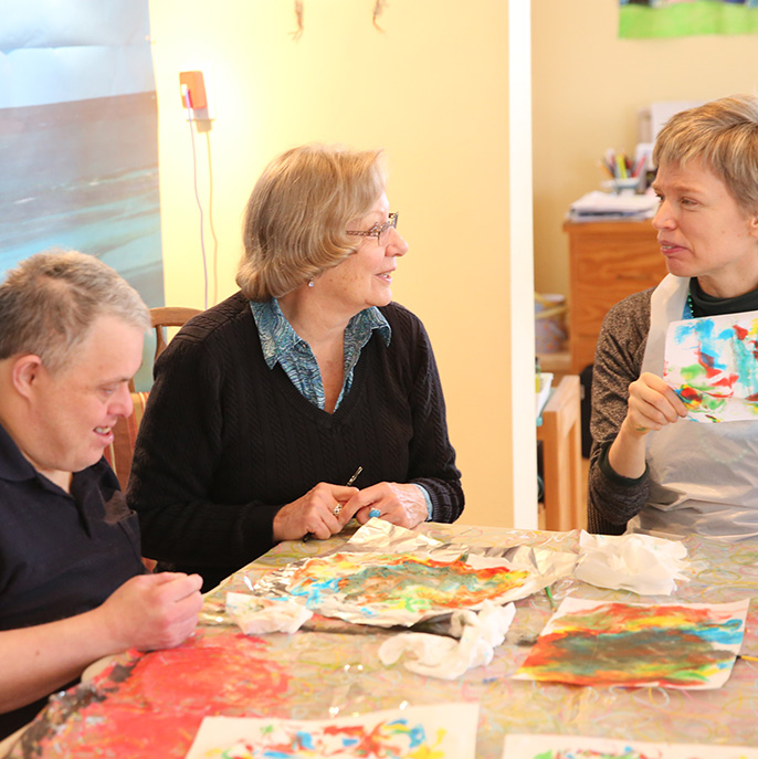 Volunteer with two people in an art activity at L'Arche