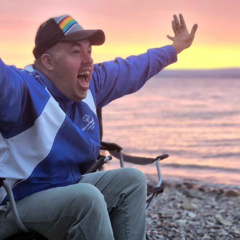 A man at the beach joyously reaching his arms out during a sunrise